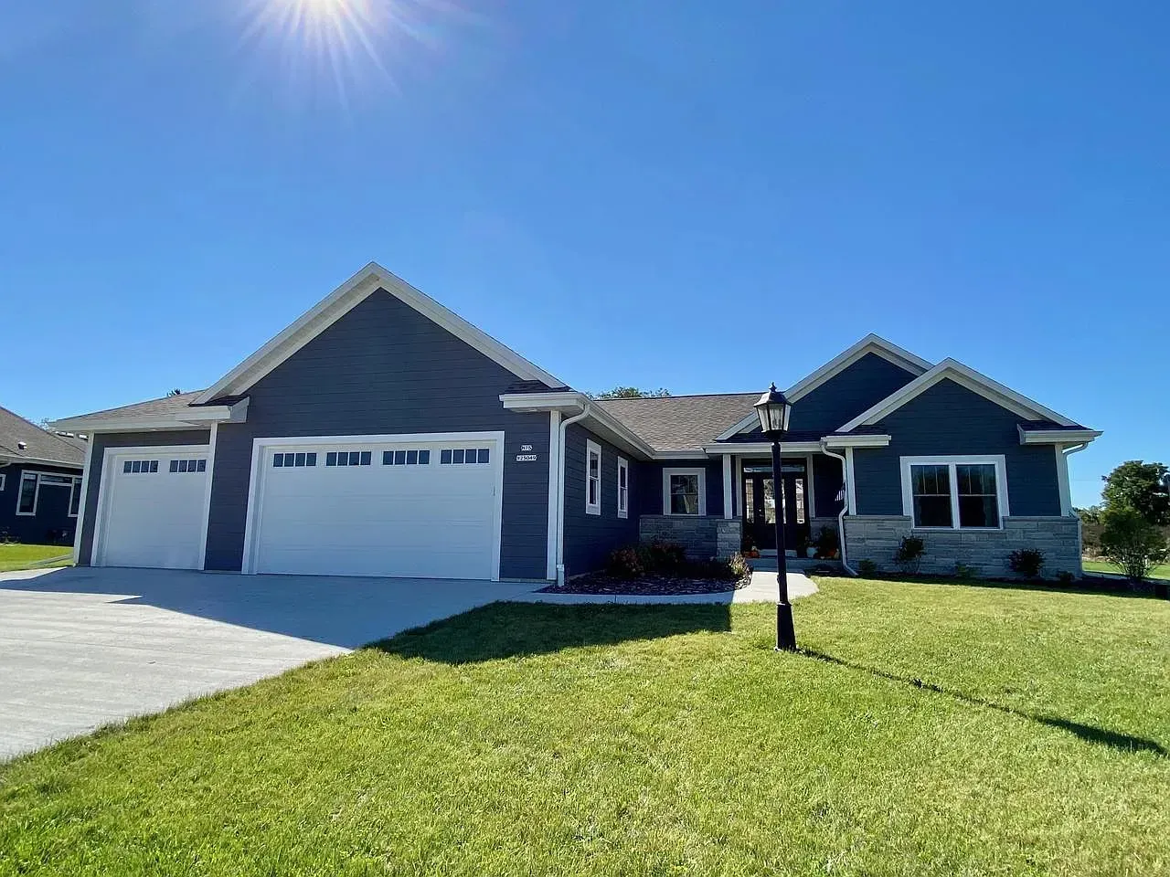 A single-story blue house with a two-car garage, white trim, and a well-manicured lawn under a bright blue sky.