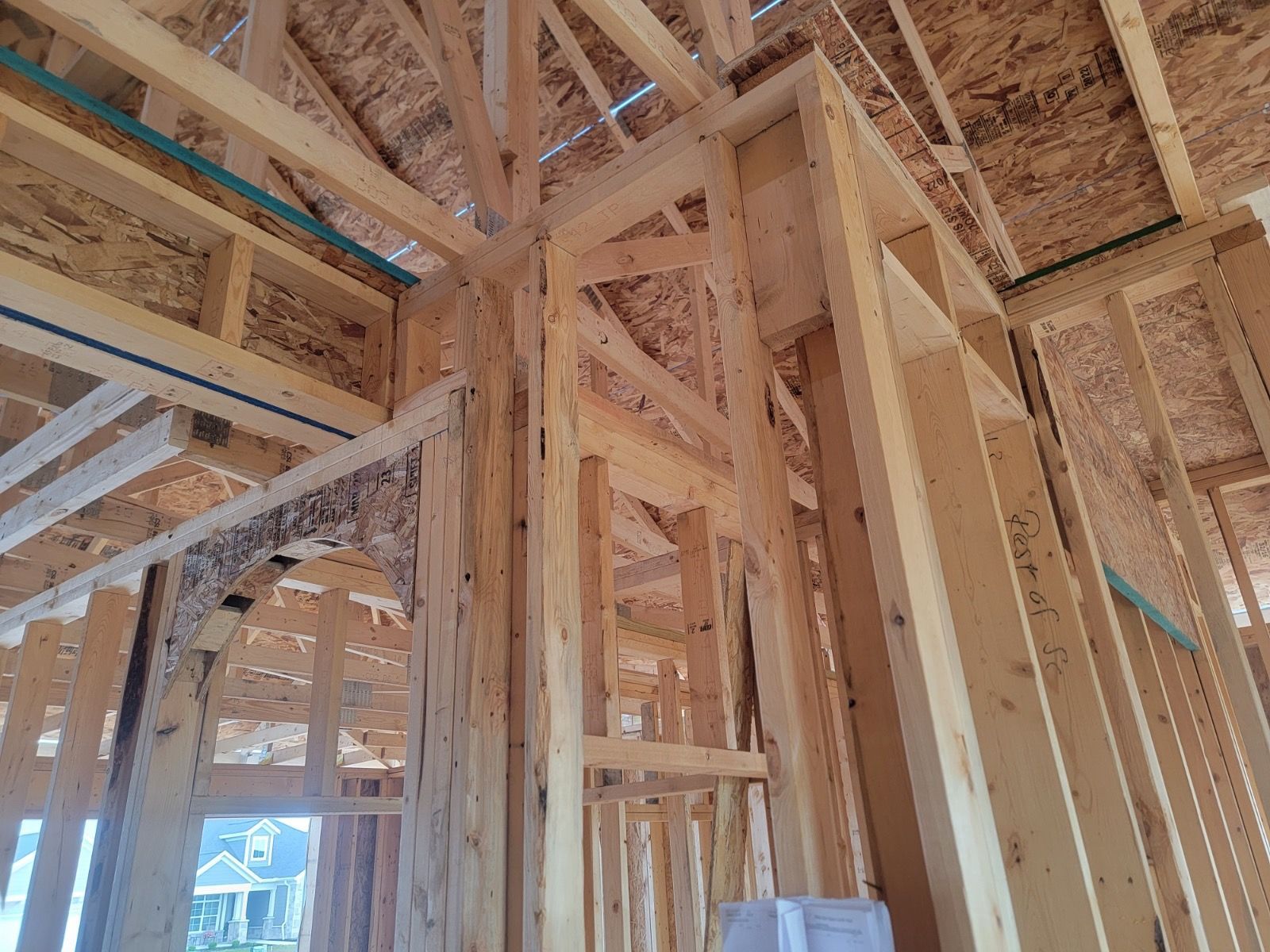 Wooden frame of a house under construction, showing walls, beams, and roof supports. Sunlight illuminates the interior.