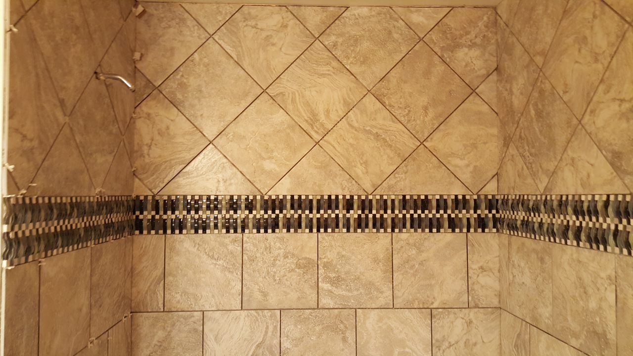 Shower walls tiled with tan squares and diamonds, with a dark band of decorative tiles across the center.