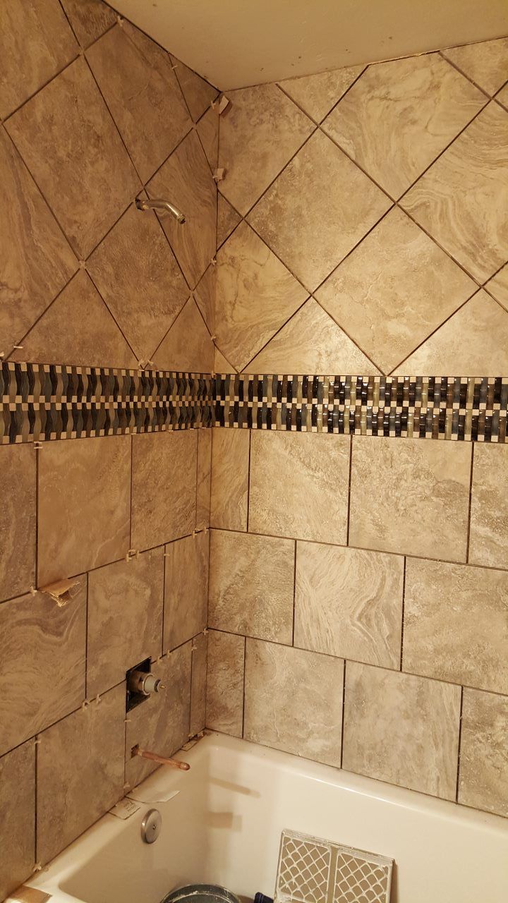 Bathroom with tan and mosaic-tiled walls, partially surrounding a white bathtub. Tiles are placed in both a vertical and diamond pattern.