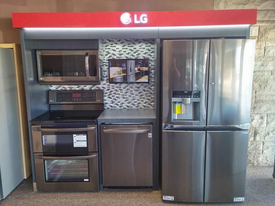 LG kitchen appliances display: microwave, oven, dishwasher, refrigerator, stainless steel, under a red LG sign.