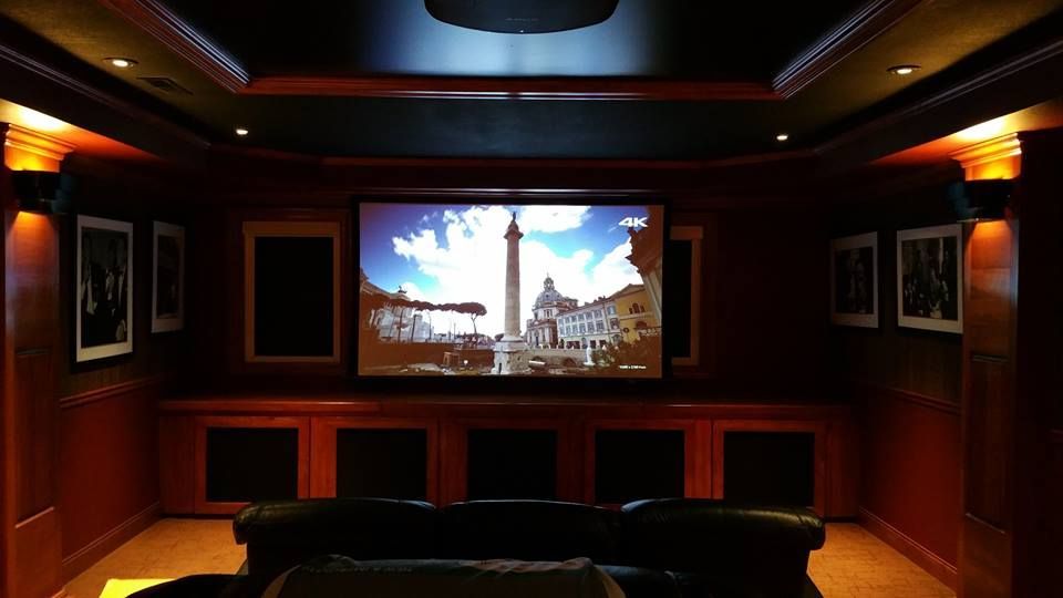 Home theater with a screen displaying a cityscape, dark wood paneling, and a black couch.