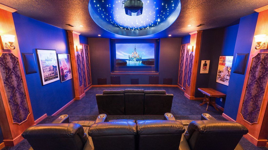 A luxurious home theater with blue walls, star-lit ceiling, and black leather recliners.