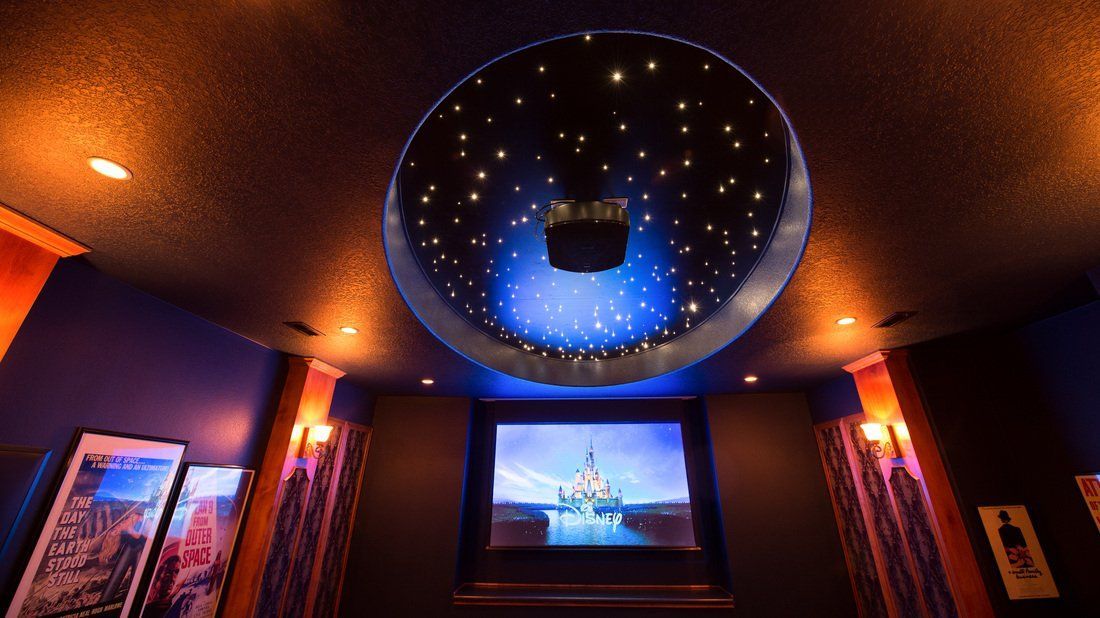 Home theater room with star-lit ceiling and a movie screen. Dark walls, warm lighting, and a projector.