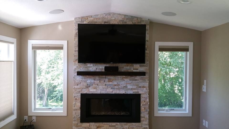 Fireplace with TV above, framed by stone, flanked by windows.