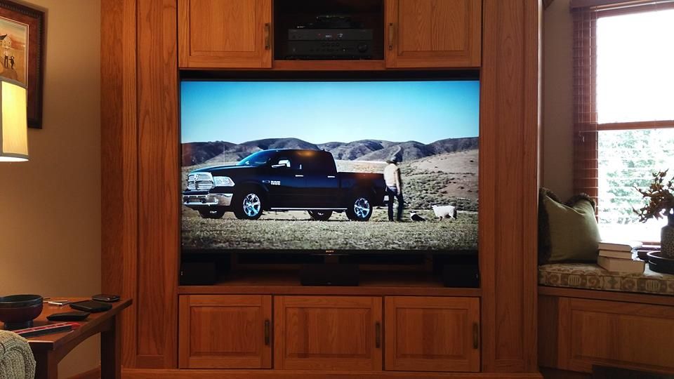 Large TV screen showing a black truck in a desert landscape, set in a wooden entertainment center.