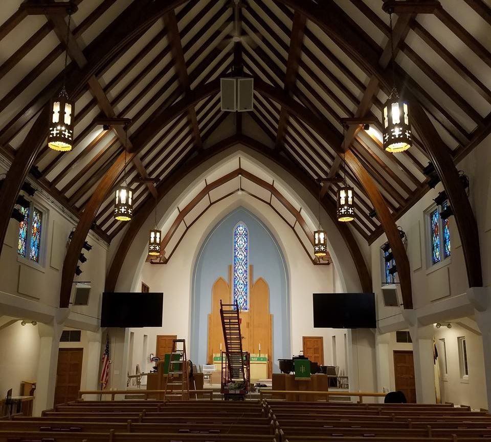 Interior of a church with a vaulted ceiling, stained glass, and wooden pews.