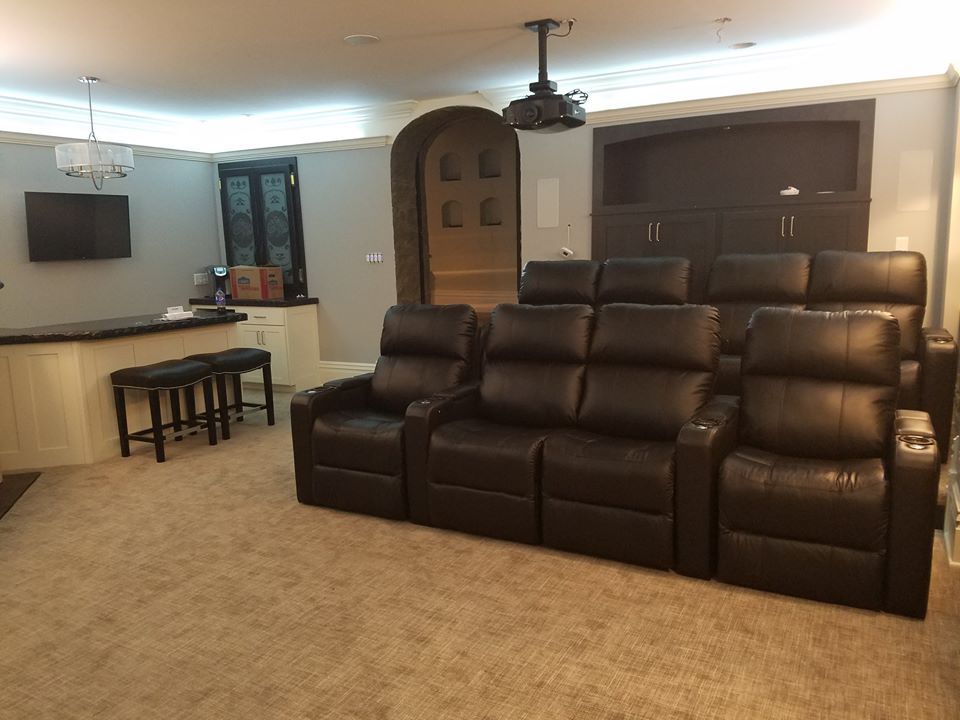 Home theater: row of black leather recliners facing a projector screen. Bar area on the left.