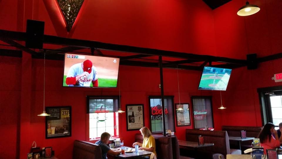 Red-walled sports bar with TVs displaying baseball. People sit at tables, eating and watching.