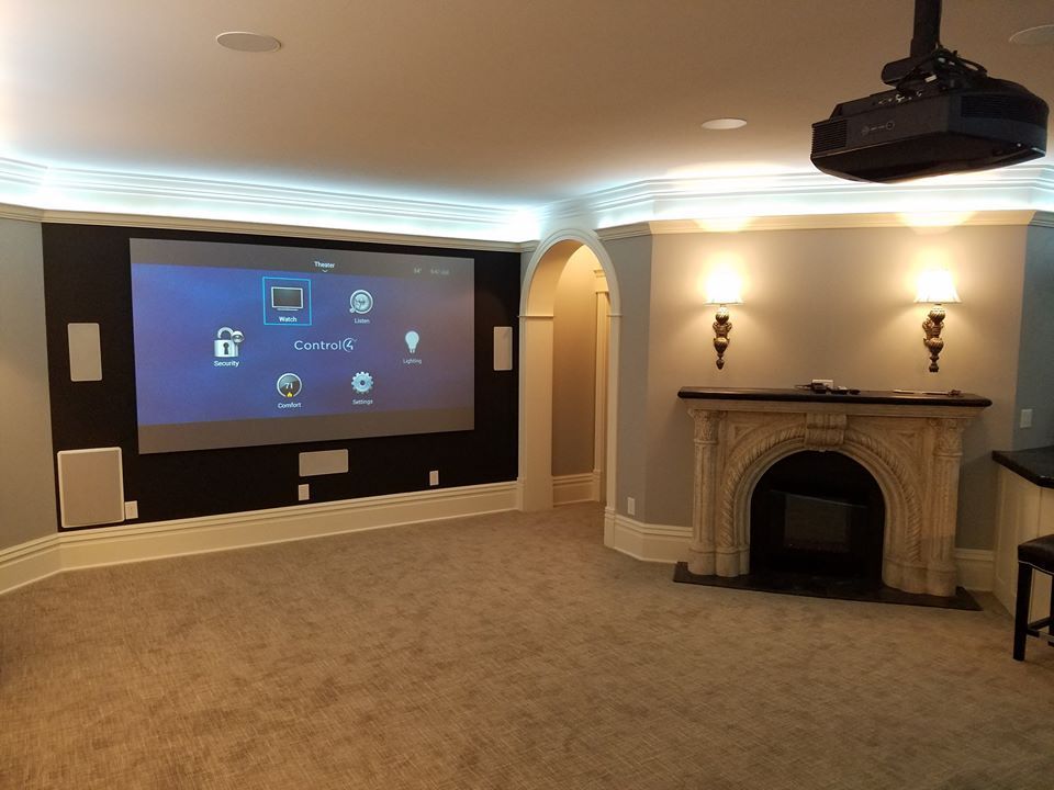 Home theater with large screen, speakers, projector, fireplace, and beige carpet.