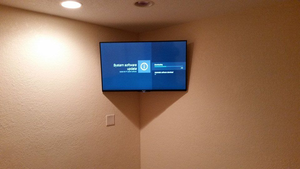 TV mounted in corner displaying a login screen, lit by a ceiling light, on tan walls.