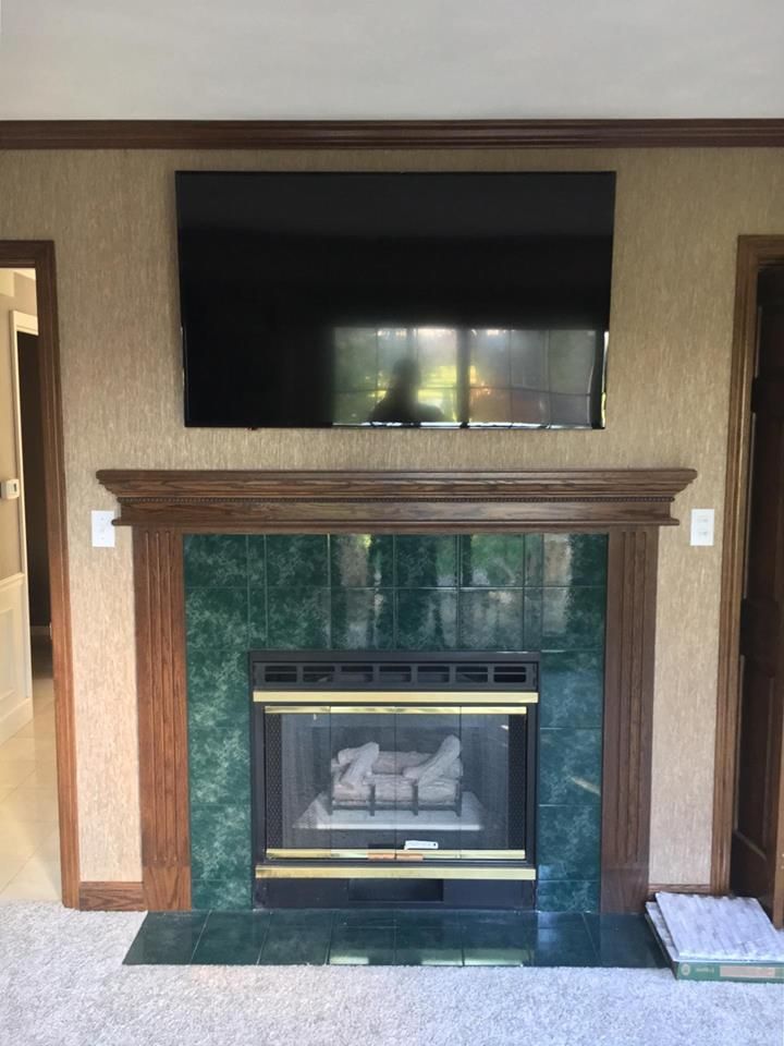 TV mounted above a fireplace with green tile, brown wood trim, and beige wallpaper.