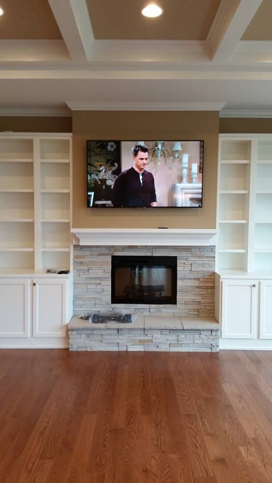 Living room with fireplace, TV, built-in bookshelves, and hardwood floors.  TV shows a man in a suit.