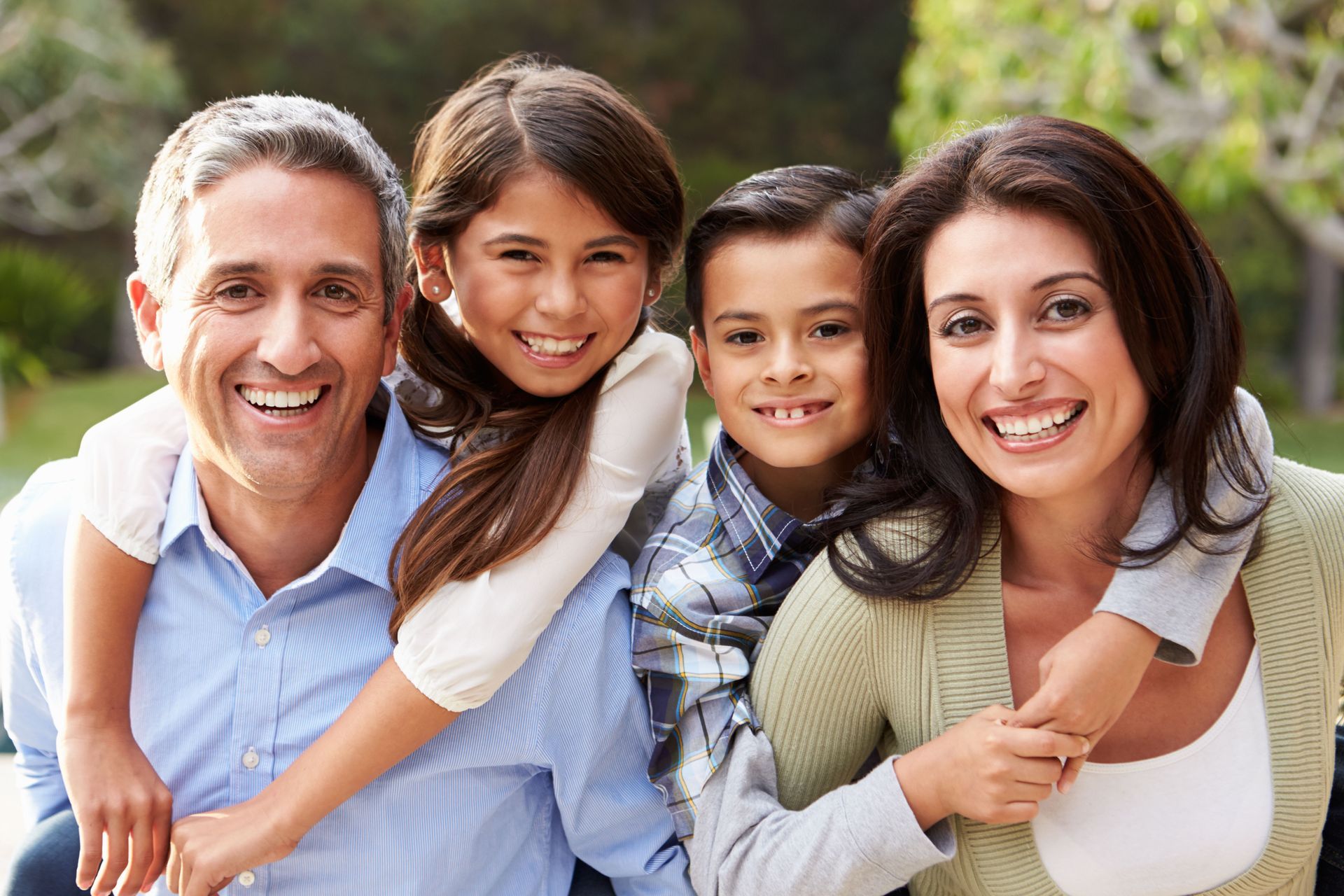 Family of four smiling outdoors, embracing.