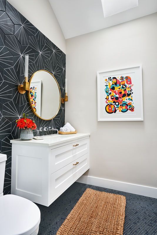 Powder room with patterned black wall, white vanity, gold mirror and colorful art.