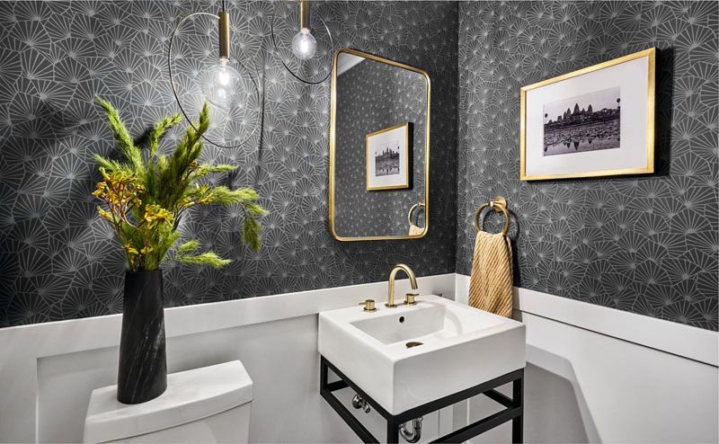 Small bathroom with black starburst wallpaper, gold accents, and a white sink.