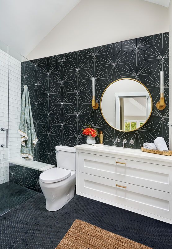 Modern bathroom with black geometric tile accent wall, white vanity, and a round mirror.