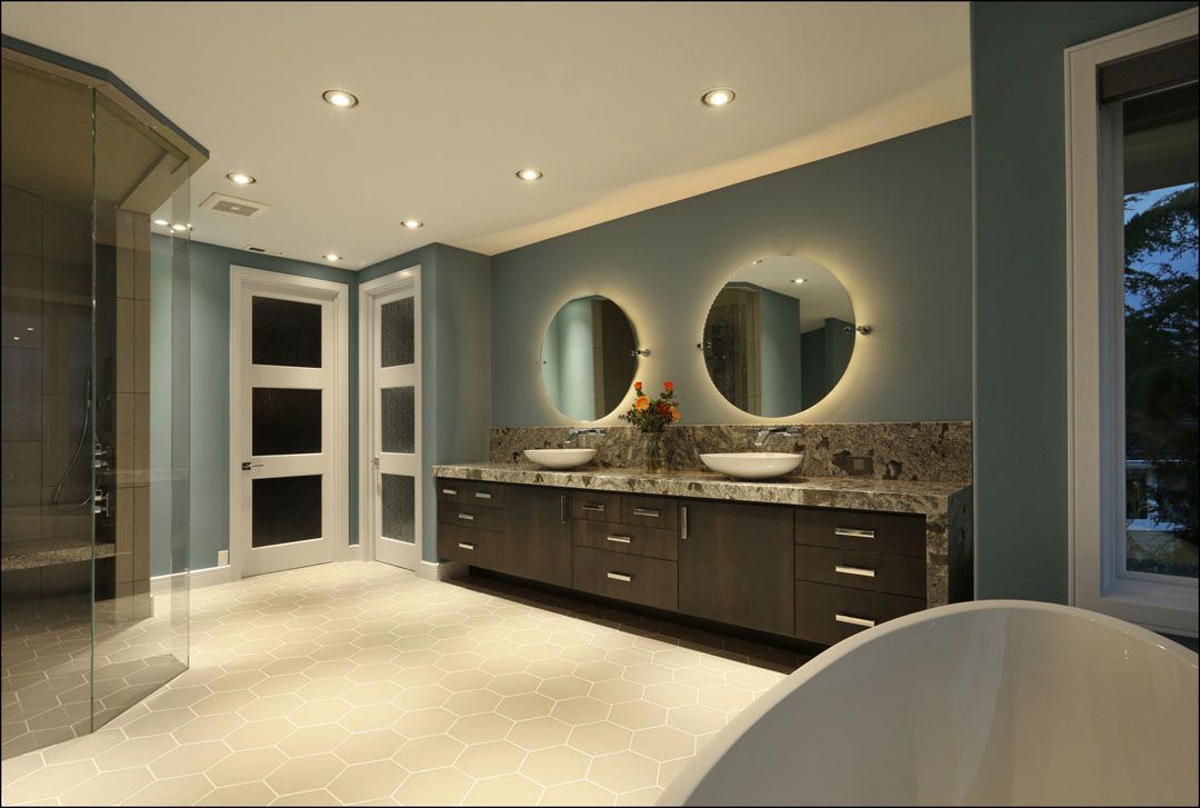 Spacious modern bathroom with blue walls, dark wood vanity, round illuminated mirrors, and a glass shower.