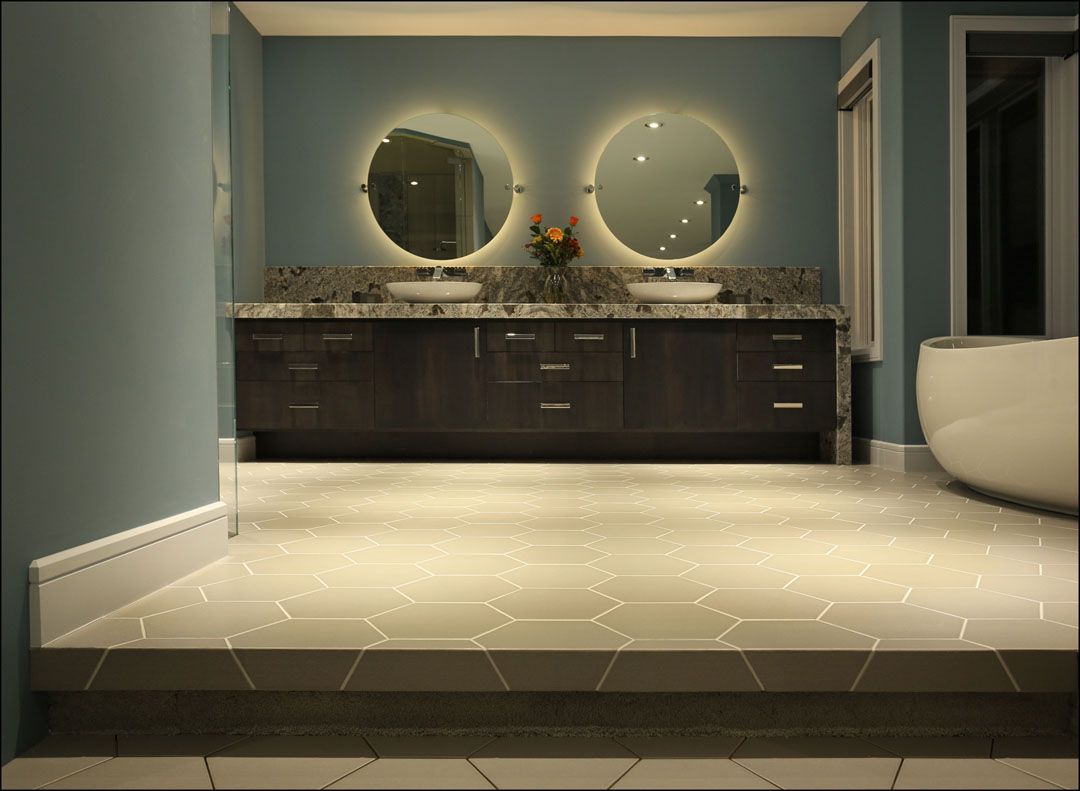 Bathroom with two illuminated round mirrors above a dark wooden vanity with sinks; teal walls, neutral tile.