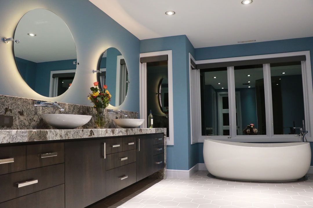 Modern bathroom with blue walls, large mirrors, dark vanity, and a white soaking tub.