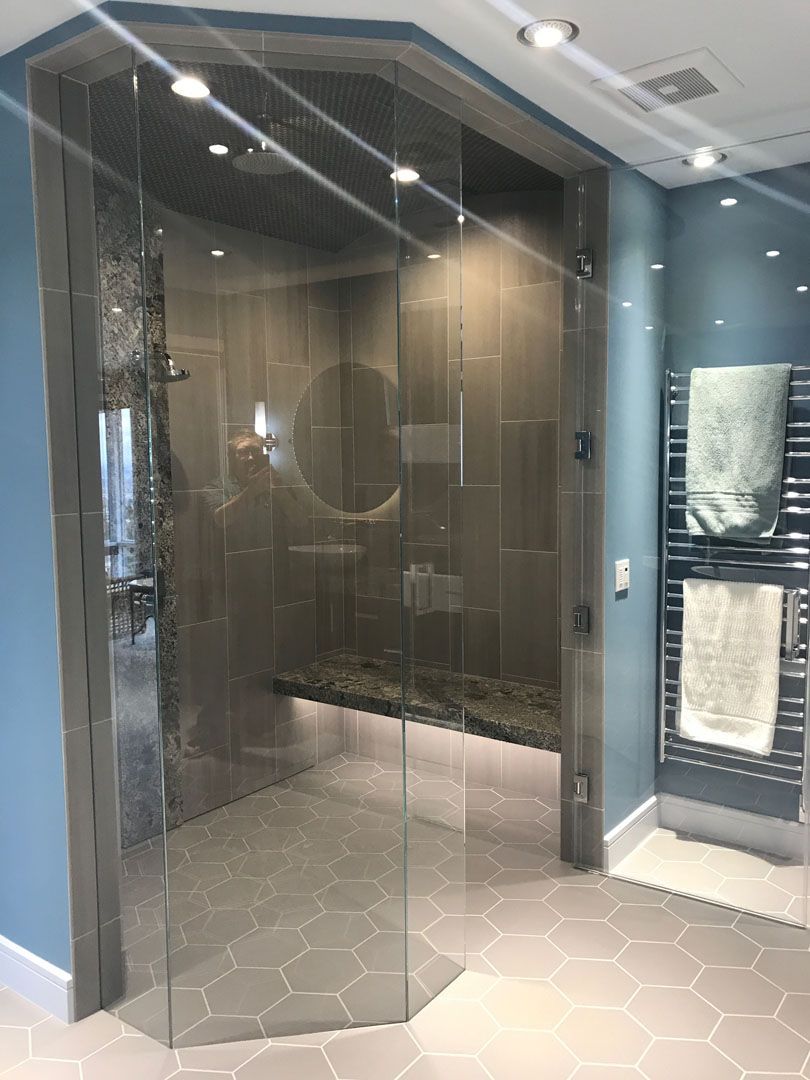 Modern shower with glass doors, gray tile walls, built-in bench, and a towel warmer on a blue wall.