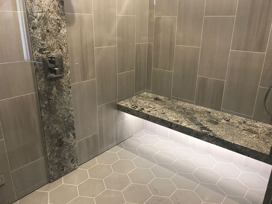 Shower with gray tiles, granite bench, and hexagon floor tiles.