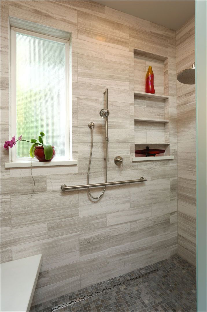 Accessible shower with grab bar, built-in shelves, window, and neutral-toned tile.