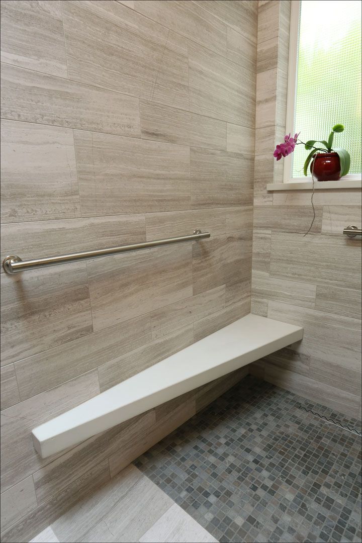 Shower with beige tile, a built-in bench, and a grab bar for accessibility.  Window with a plant.