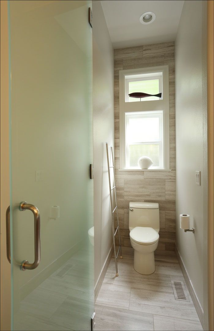Narrow bathroom with frosted glass door and toilet in front of window with decorative fish.