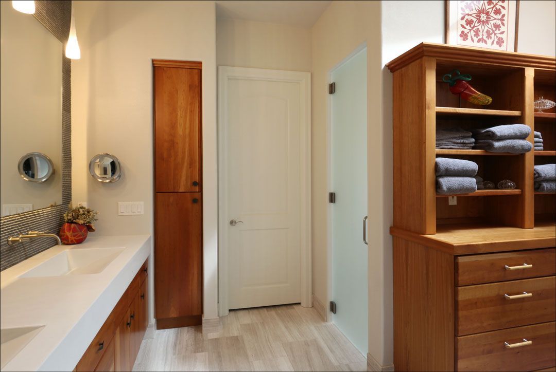 Bathroom with light wood storage, a tall cabinet, white door, and sink.