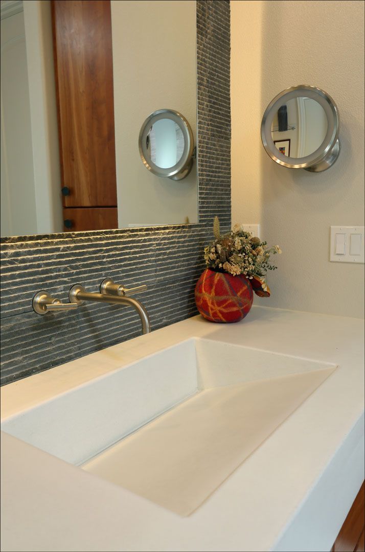 Modern bathroom with white sink, bronze faucet, blue-grey tile backsplash, round mirrors, and flower arrangement.