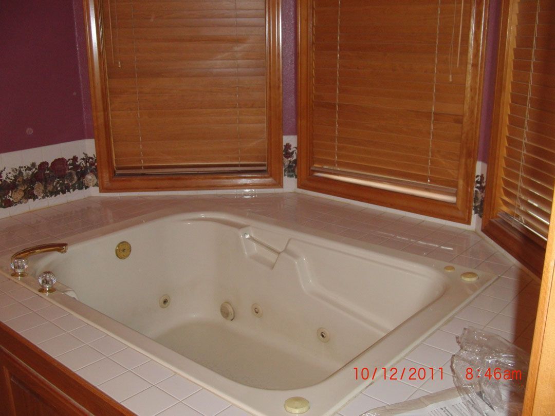 A corner jacuzzi tub in a bathroom with wooden blinds above.