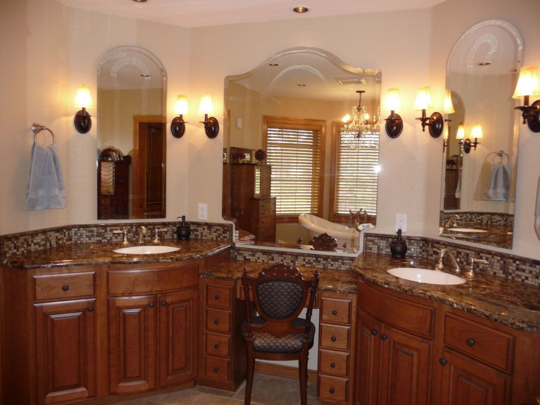 Bathroom with dark wood vanities, granite countertops, arched mirrors, and sconces.
