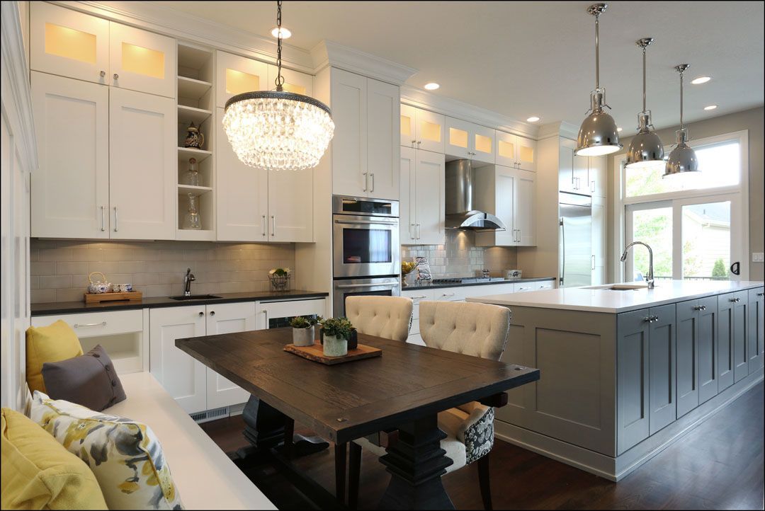 Modern kitchen with white cabinets, dark island, dining table, and pendant lights.