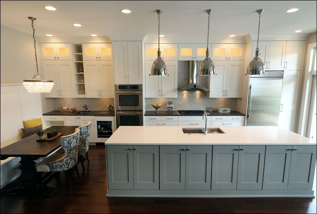 Modern white kitchen with island, pendant lights, stainless steel appliances, and dark wood floors.
