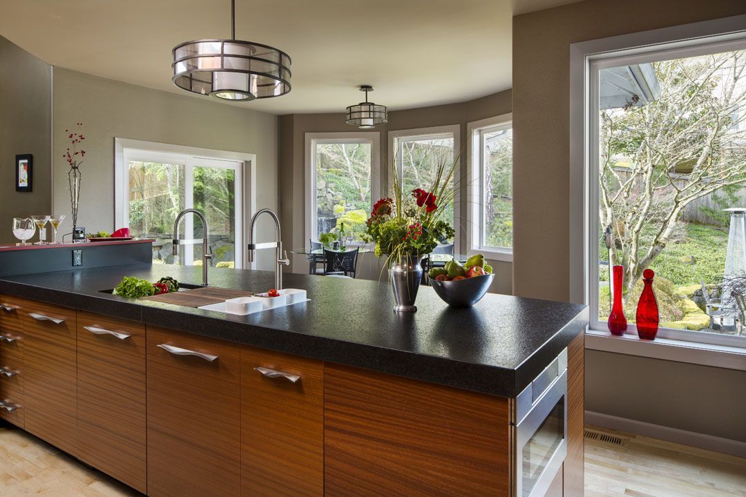 Modern kitchen with wooden island, dark countertop, and large windows overlooking greenery.
