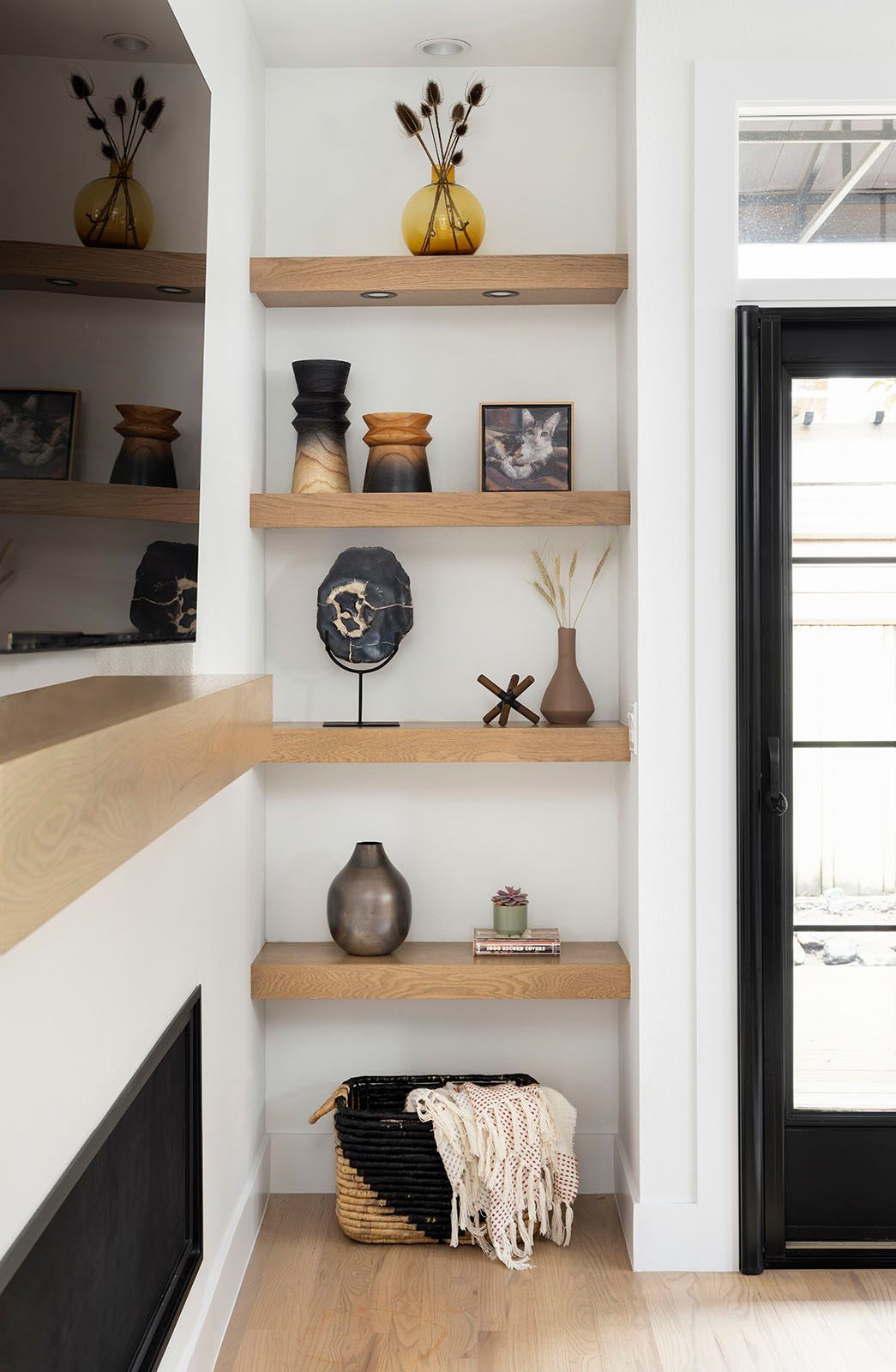 Wooden shelves with decor against white wall. Basket with blanket on the bottom shelf
