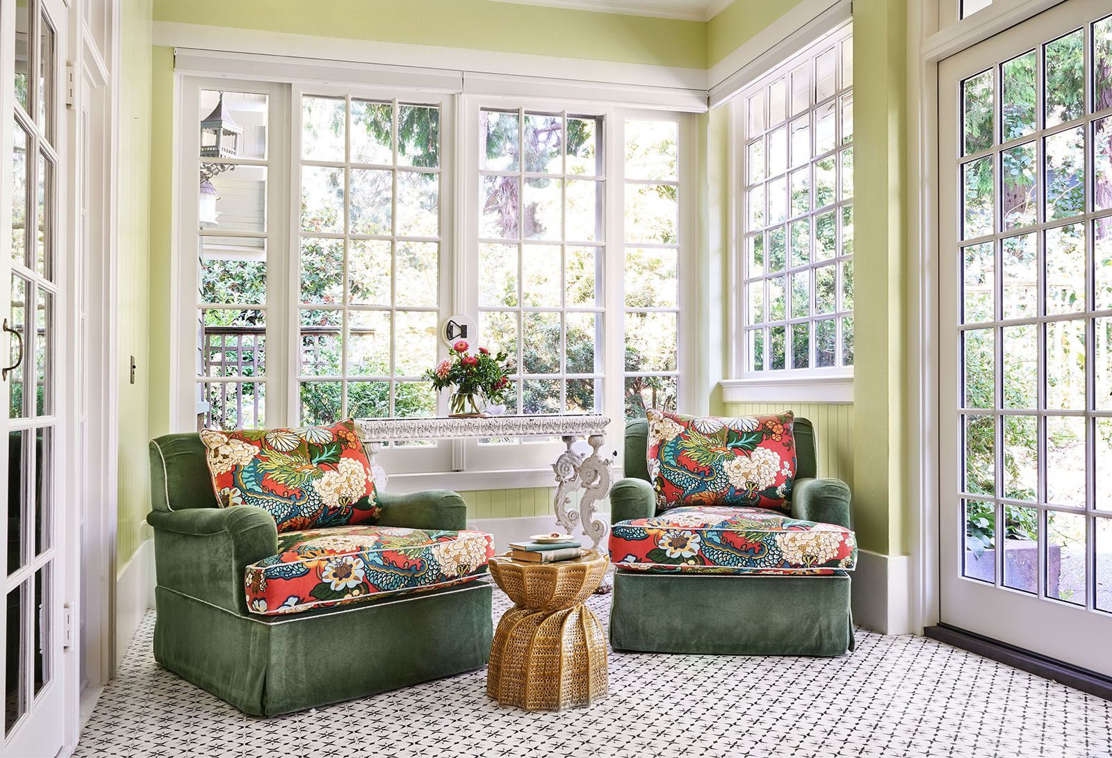 Sunroom with green armchairs and floral cushions, white windows, and a small table