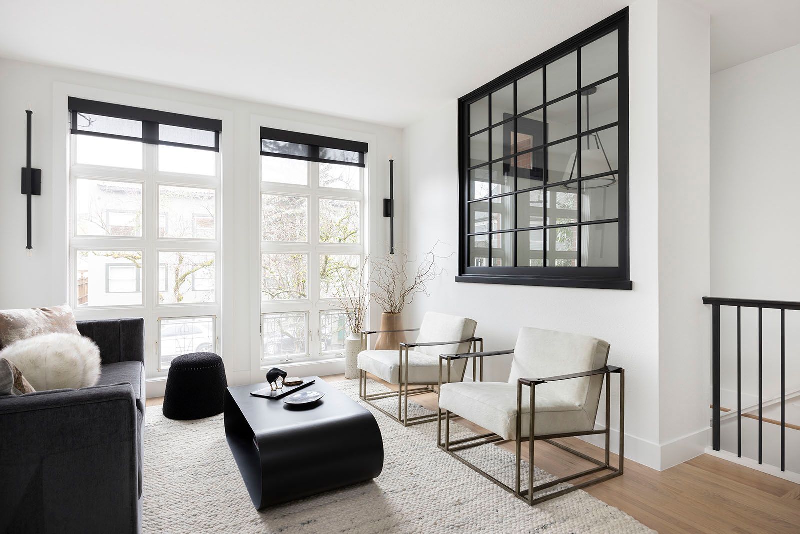 Modern living room with black and white decor, large windows, and a black grid mirror