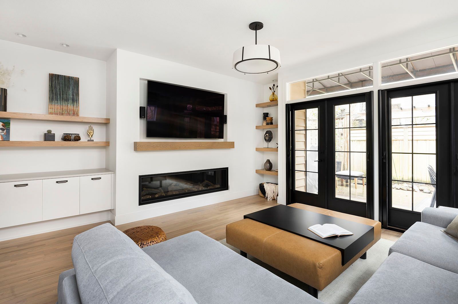 Modern living room with fireplace, built-in shelves, TV, and black doors leading outside