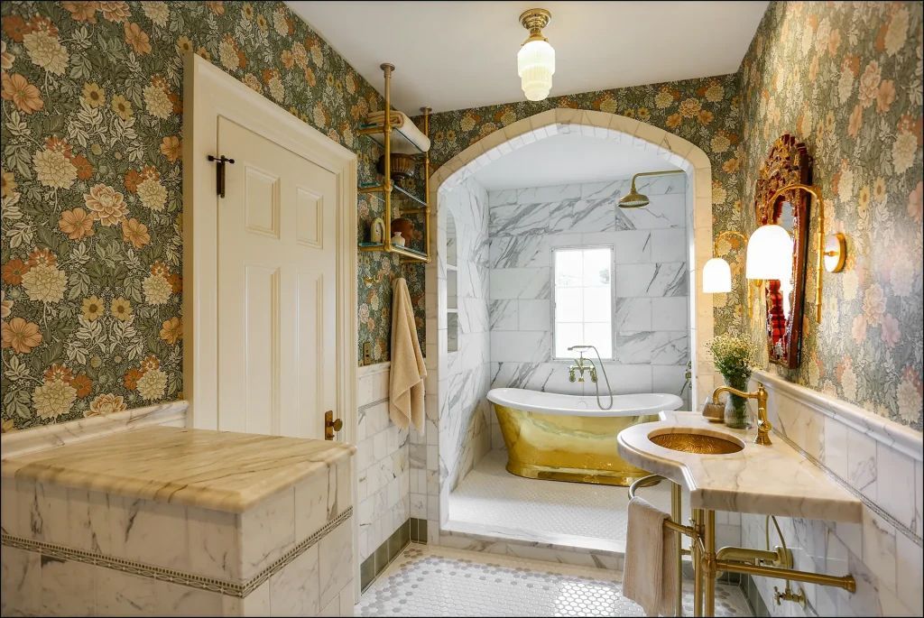 Floral wallpapered bathroom with marble accents, gold fixtures, and a clawfoot tub.