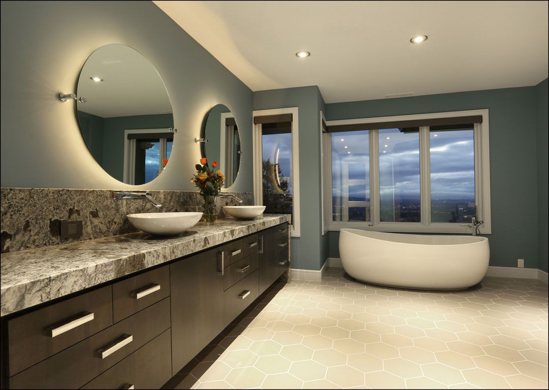 Modern bathroom with blue walls, a white tub by the window, and a dark wood vanity with two sinks