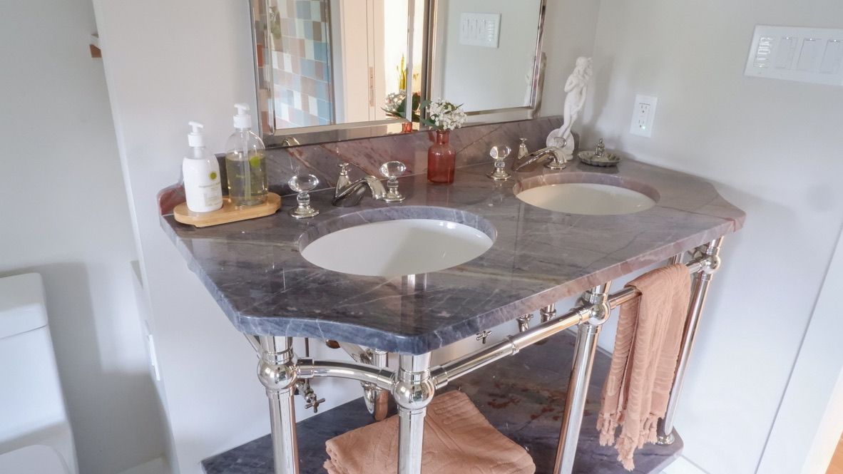 Vanity with two sinks, granite countertop, ornate metal frame, towels, and mirror.