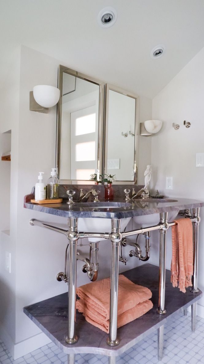 Open bathroom with a silver-framed double vanity, mirrors, towels, and white walls.