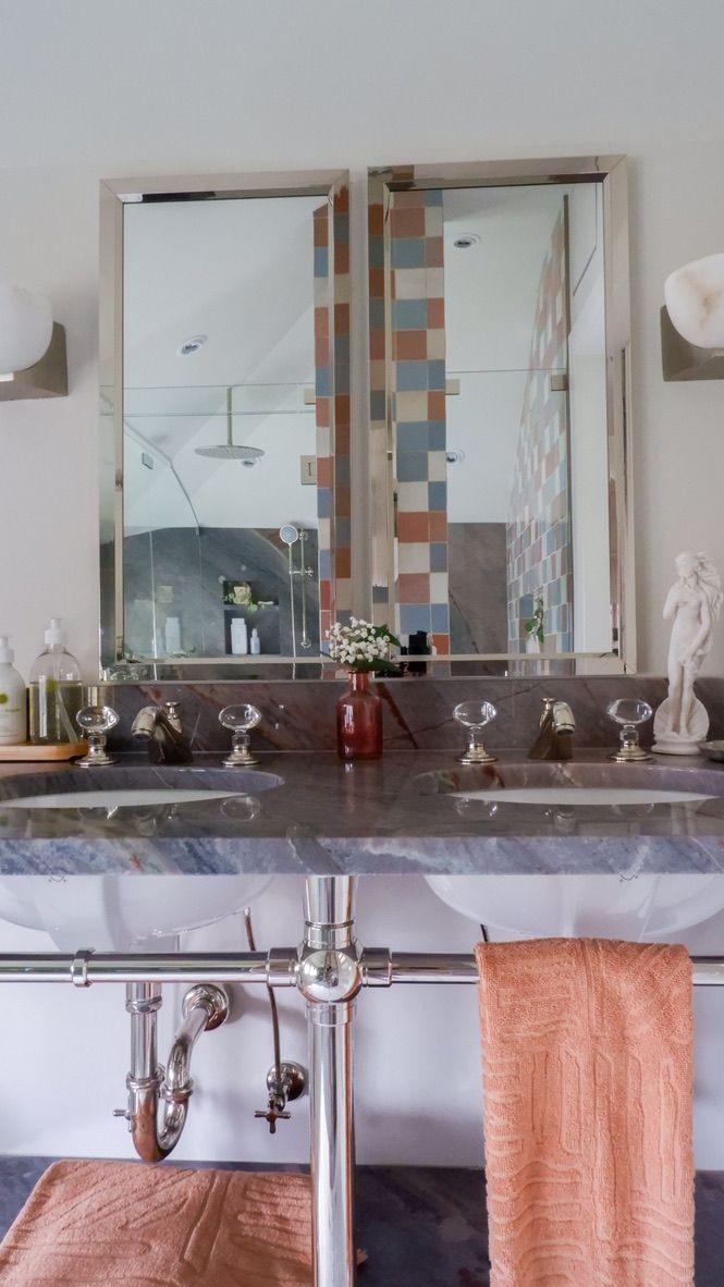 Bathroom with double sinks, framed mirrors, and colorful backsplash tile. Peach towel hangs below.