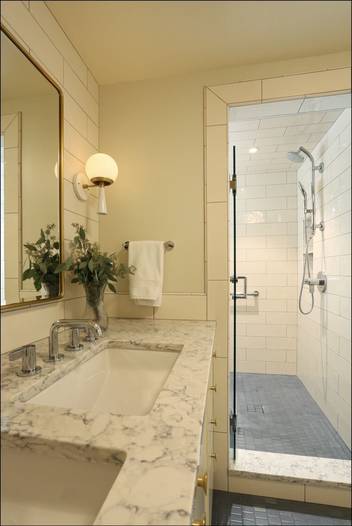 Bathroom with white marble countertop, glass shower, and gold fixtures.