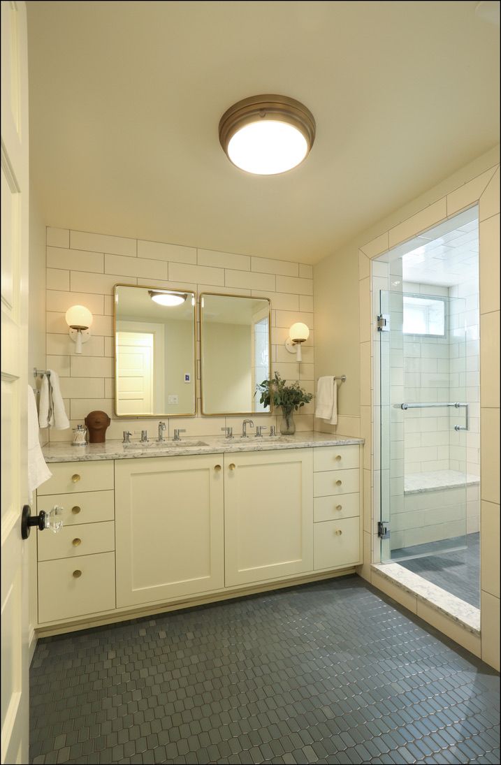Bathroom with white vanity, two mirrors, glass shower, dark floor tiles.