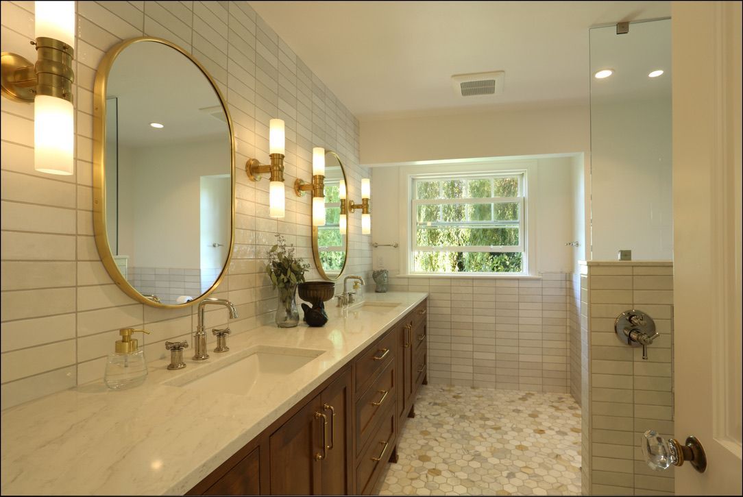 Bathroom with gold-framed oval mirrors, sconces, and a marble countertop above a wooden vanity.