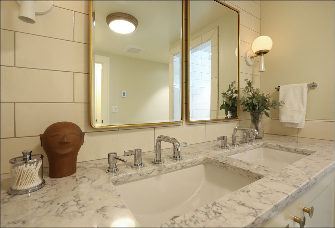 Bathroom with a double sink, gold mirrors, and marble countertop.
