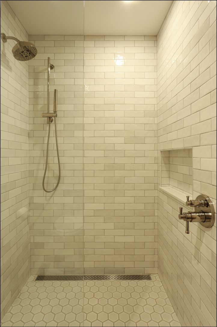 Shower with white rectangular tiles and hexagonal floor, glass door, and brushed metal fixtures.